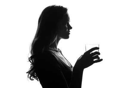 Silhouette of handsome woman with long hair with glass in her hand. She stays side to camera and looks stright. Cut-out scene. Studio shotの写真素材