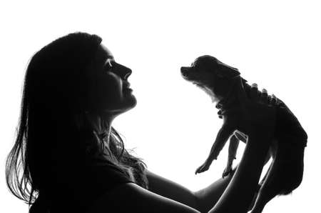 Silhouette of handsome woman standing with smal dog in her hands. She lifted pet over the head. Cut-out scene. Studio shot.の写真素材