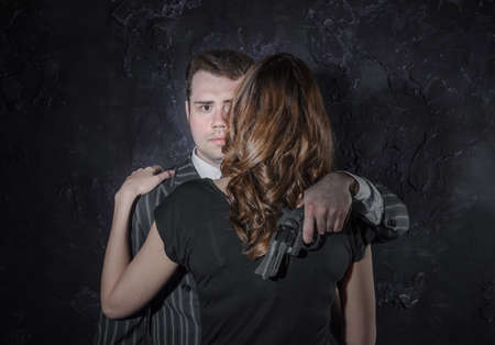 A detective with a gun and his beautiful woman in retro outfit leaning on him. Studio shot. Noir style. Studio shotの写真素材