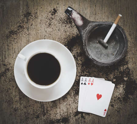 game abstract: coffee cup, ashtray with cigarette and four aces playing cards on the wooden backgroundの写真素材