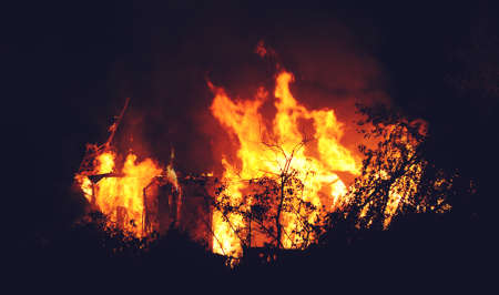 Arson or nature disaster - burning fire flame on wooden house roofの写真素材
