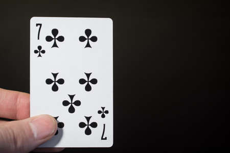 Abstract: man hand holding playing card seven of clubs on a black background with copyspaceの写真素材