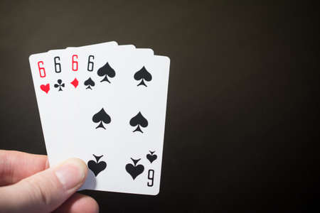 Man hand holding playing card four six isolated on black background with copyspace poker set four...