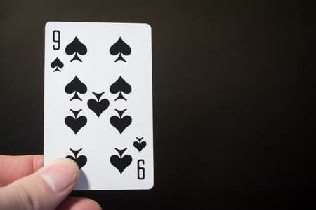 Man hand holding playing cards nine of spades isolated on black background with copyspace abstract