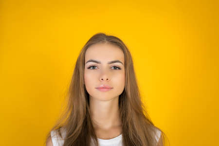 Pretty and young joyfully female with fair hair, dressed casually, looking with satisfaction at camera. Studio shot of good-looking beautiful woman isolated against yellow blank studio wall.の写真素材