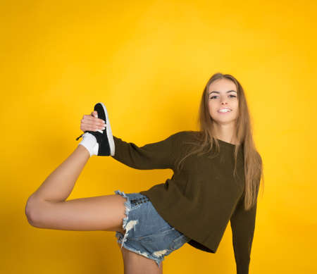 Ecstatic blond young woman in jeans shorts over yellow background