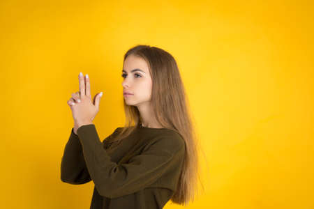 Beautiful woman in sweater is hiding hand raised and blowing at finger gun, studio shot with...