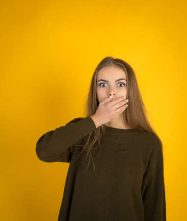 Girl covering her mouth with her hands over yellow background, studio shotの写真素材