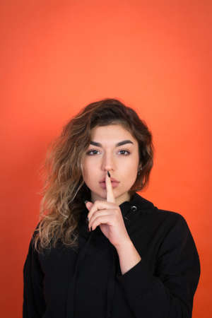 beautiful girl with curly hair in a black t-shirt on a red background looking into the camera