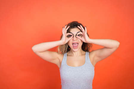 Positive young woman gesture and looking in camera, red background, studio shot