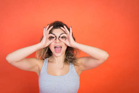 Positive young woman gesture and looking in camera, red background, studio shot