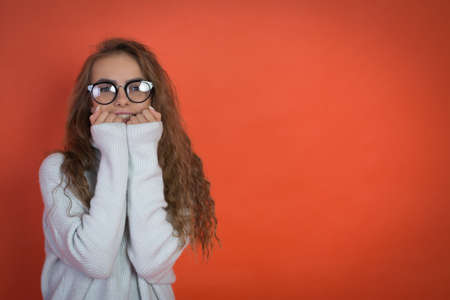 beautiful teenager girl in white sweater and glasses on red background