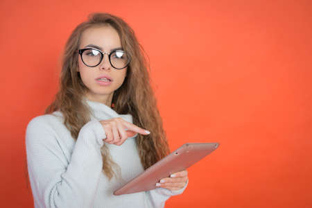 Pretty young woman holding and uses tablet on red backgroundの写真素材