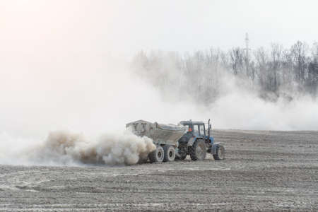 Tractor with trailer fertilizes agricultural field in spring for sowing corn or wheatの写真素材