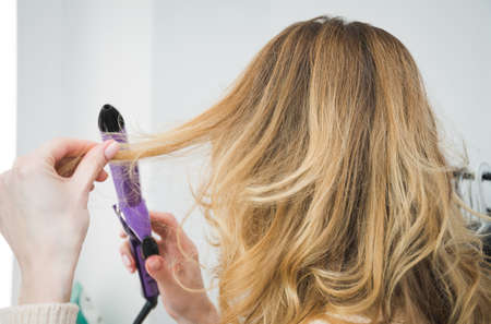 Middle aged mature woman doing her hair in the morning with heated curling tongs, beauty and fashion conceptの写真素材