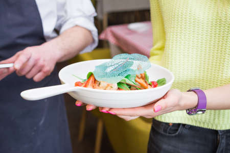 Woman hands holds salad plate in a restaurantの写真素材