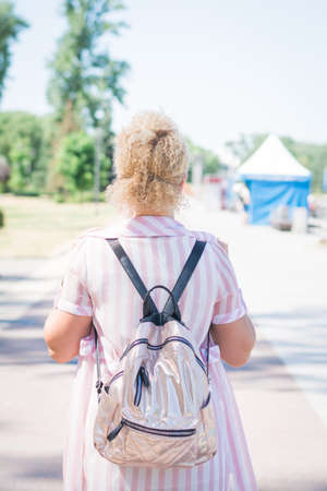 Back View Of Happy Woman With Backpack Walking In summer city Park