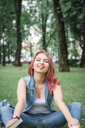 The girl with red hair in the park at a picnic reads a book and poses for the photographerの写真素材