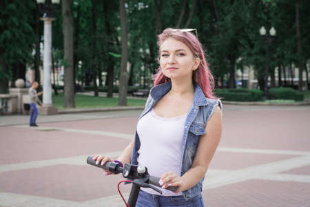 Modern beautiful young woman riding an ecological electric scooter in city street, lifestyle conceptの写真素材