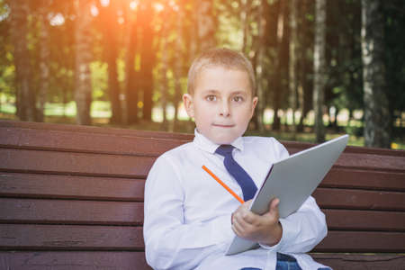 Little child schoolkid writing on a notebook with pencil while sitting on the bench in the park.の写真素材