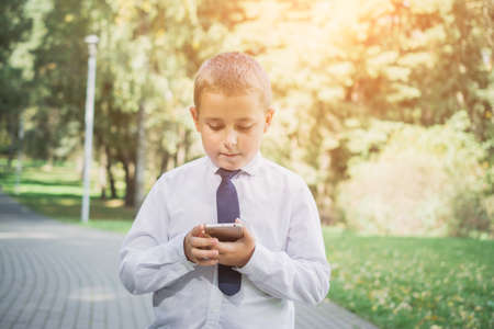 eight-year-old boy uses a smartphone in a city park, technology development conceptの写真素材