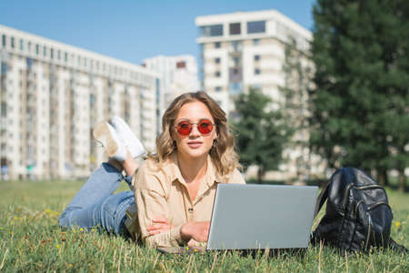 college student lying down on the grass working on laptop at campus