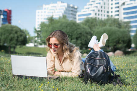 young female college student reading info on her laptop on a campus lawn