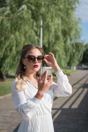 Portrait of young smiling fashion girl standing with smartphone outdoorの写真素材