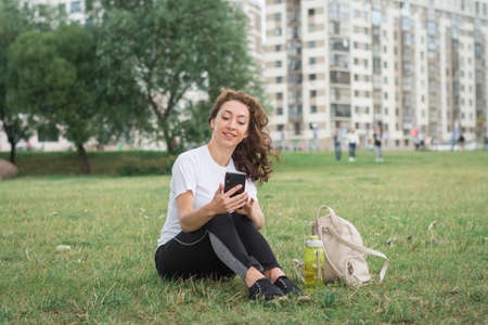 Attractive girl in casual clothes sits on the lawn in university park