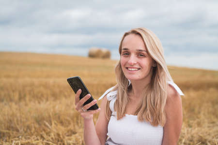 beautiful young woman in a mown wheat field with a phone in her handsの写真素材