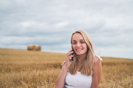 beautiful young woman in a mown wheat field with a phone in her handsの写真素材