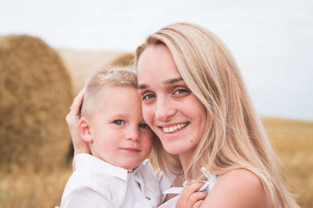 Young beautiful mother and son in white clothes posing for a photograph in a wheat field, happy family conceptの写真素材