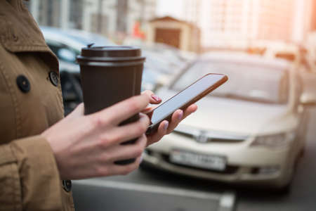 woman hands with mobile phone and big coffee cup on city streetの写真素材