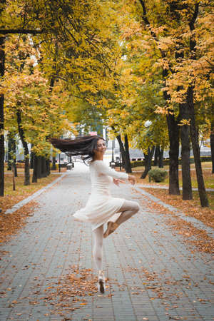 Girl ballerina in a white dress dancing in the autumn city parkの写真素材