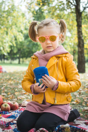 portrait of a little beautiful three-year-old girl who plays in the autumn parkの写真素材