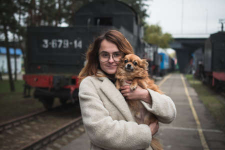 Portrait of a young girl in glasses with a small dog in her arms on the railway platform of the old stationの写真素材
