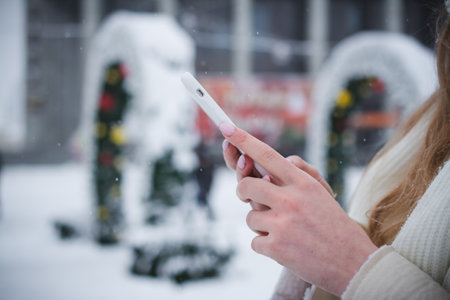 Hands of a girl and a telephone in winter on the background of the city landscapeの写真素材