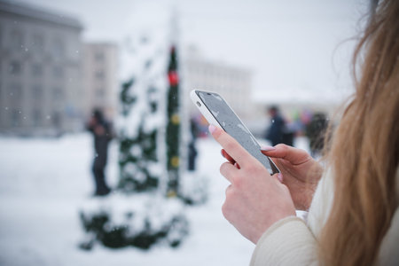 Hands of a girl and a telephone in winter on the background of the city landscapeの写真素材