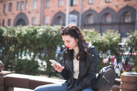 Young cheerful stylish woman using cell phone and texting message on city streetの写真素材