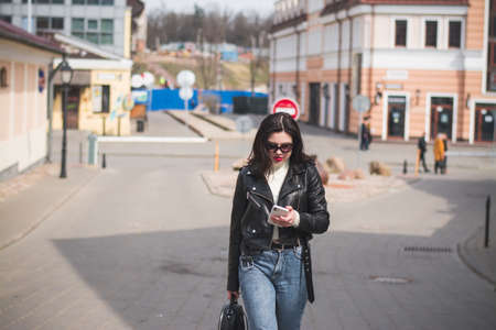 A beautiful hipster girl with a phone in her hands walks down the streetの写真素材