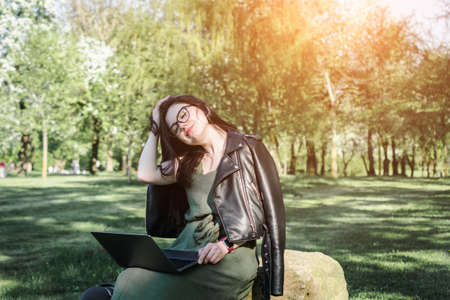 A student caucasian girl with the laptop sitting on the grass a summer day
