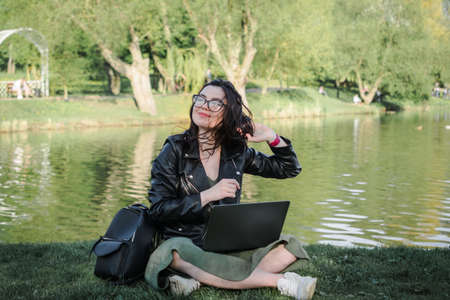 A student caucasian girl with the laptop sitting on the grass a summer dayの写真素材