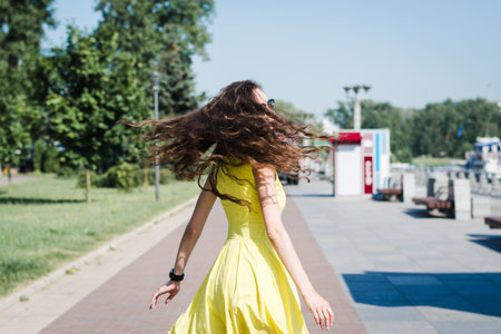Beautiful girl in a yellow dress walks in a summer park on a sunny morningの写真素材