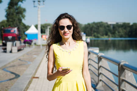 Beautiful girl in a yellow dress walks in a summer park on a sunny morningの写真素材