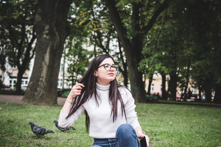 Beautiful stylish girl in jeans and a white sweater outdoors in the park with a phone in her handsの写真素材