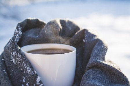 White mug with hot coffee in the snow in winterの写真素材