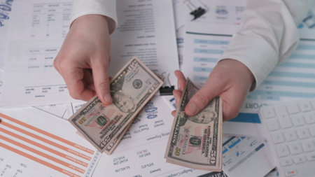 Hands counting dollars closely against the background of financial reportsの写真素材