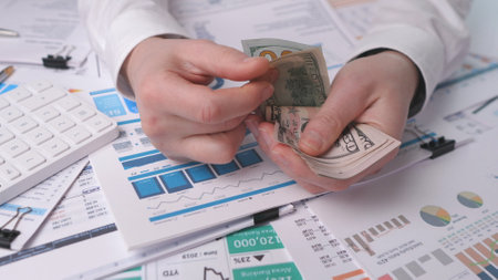 Hands counting dollars closely against the background of financial reportsの写真素材