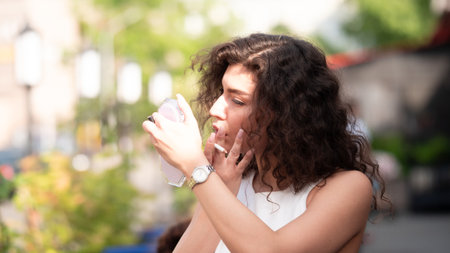 Beautiful girl with long curly hair in a white T-shirt with a cup of coffee on the street