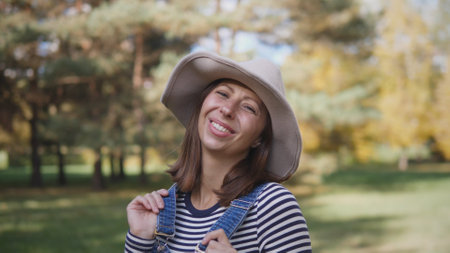 A Cheerful Woman Smiling Brightly in a Beautiful Autumn Landscape Wearing a Stylish Hatの写真素材